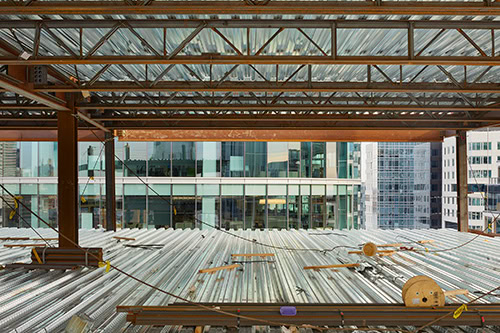 Steel joist floor system under construction with open-web steel joists, metal roof deck, and structural steel framing in a commercial multi-story building.
